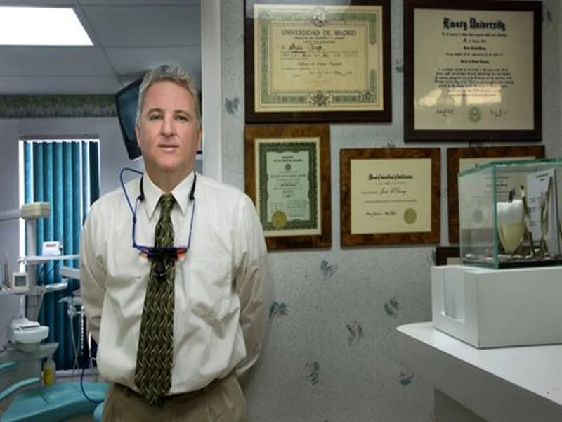 Dr. Brian Dewey standing in his dental office with diplomas behind him
